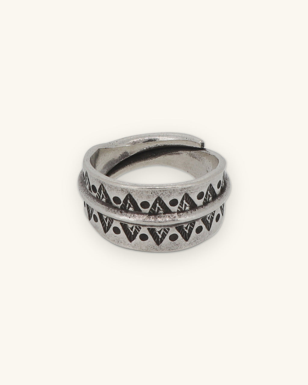 Wide silver wrap band ring stamped with triangles and dots on either side of a raised ridge, shown on a sand background