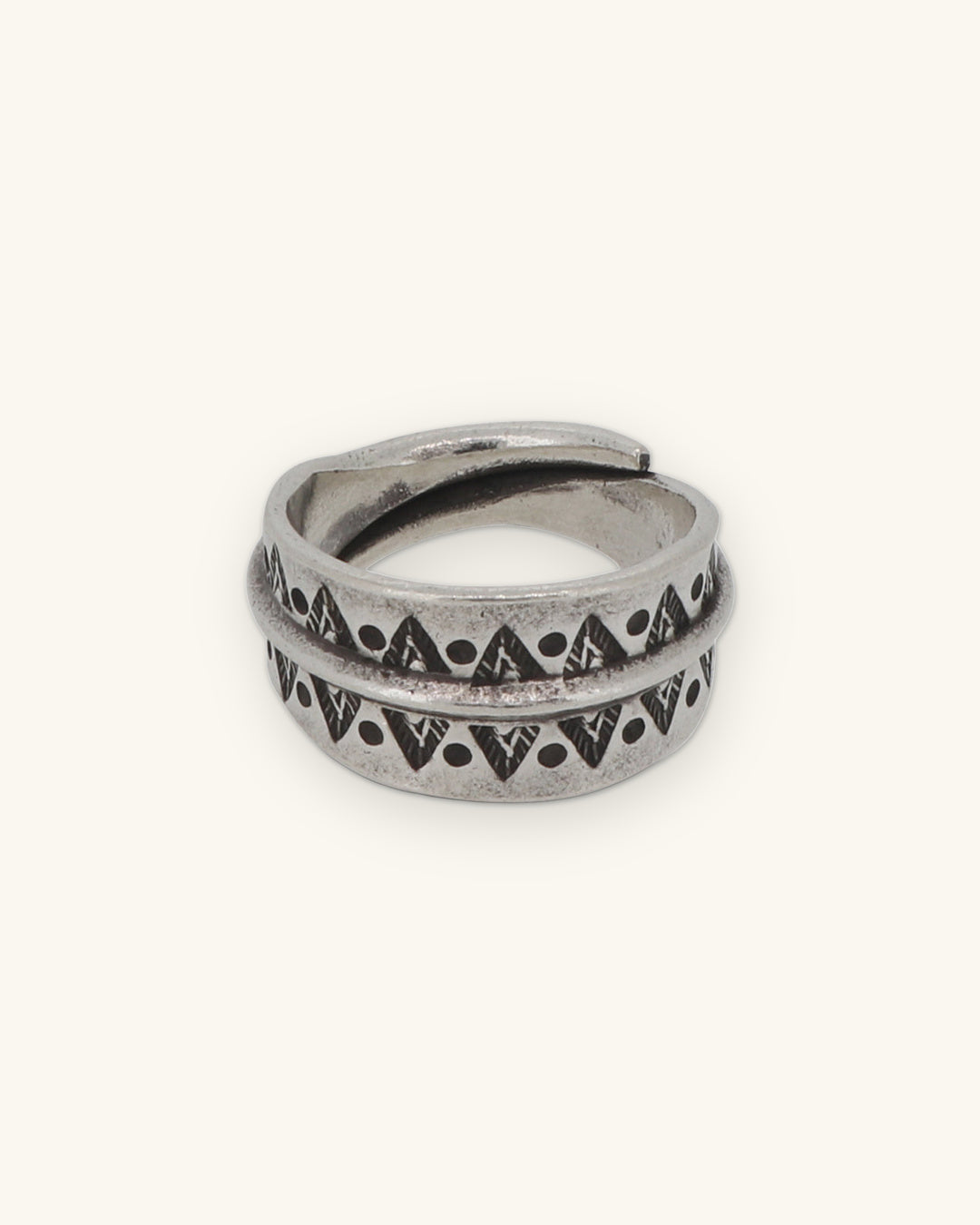 Wide silver wrap band ring stamped with triangles and dots on either side of a raised ridge, shown on a sand background