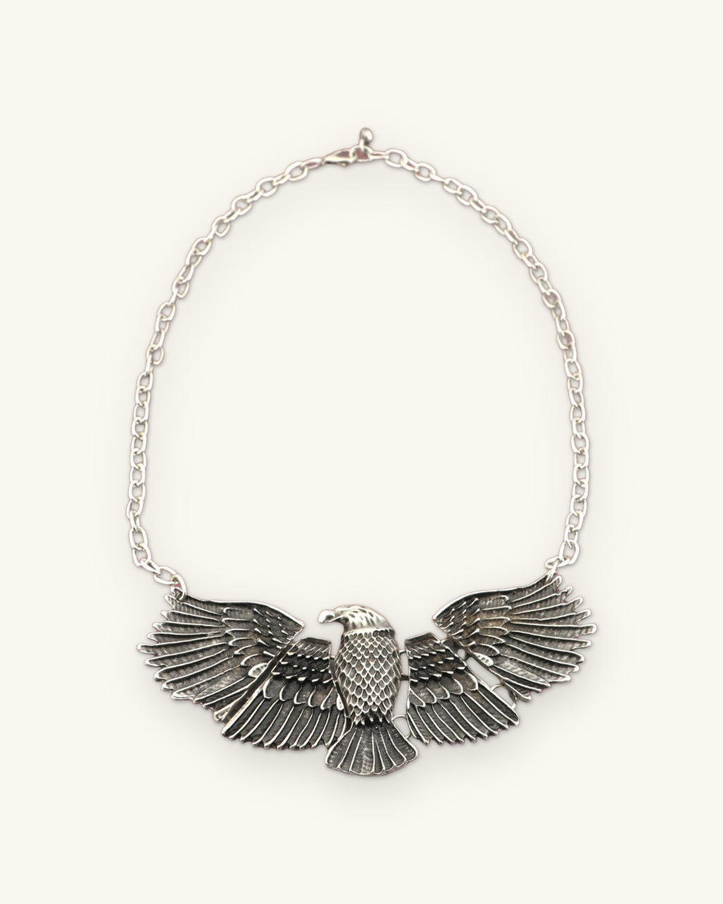 Eagle pendant necklace laid flat with the full cable chain and clasp, front view, shown on a sand background