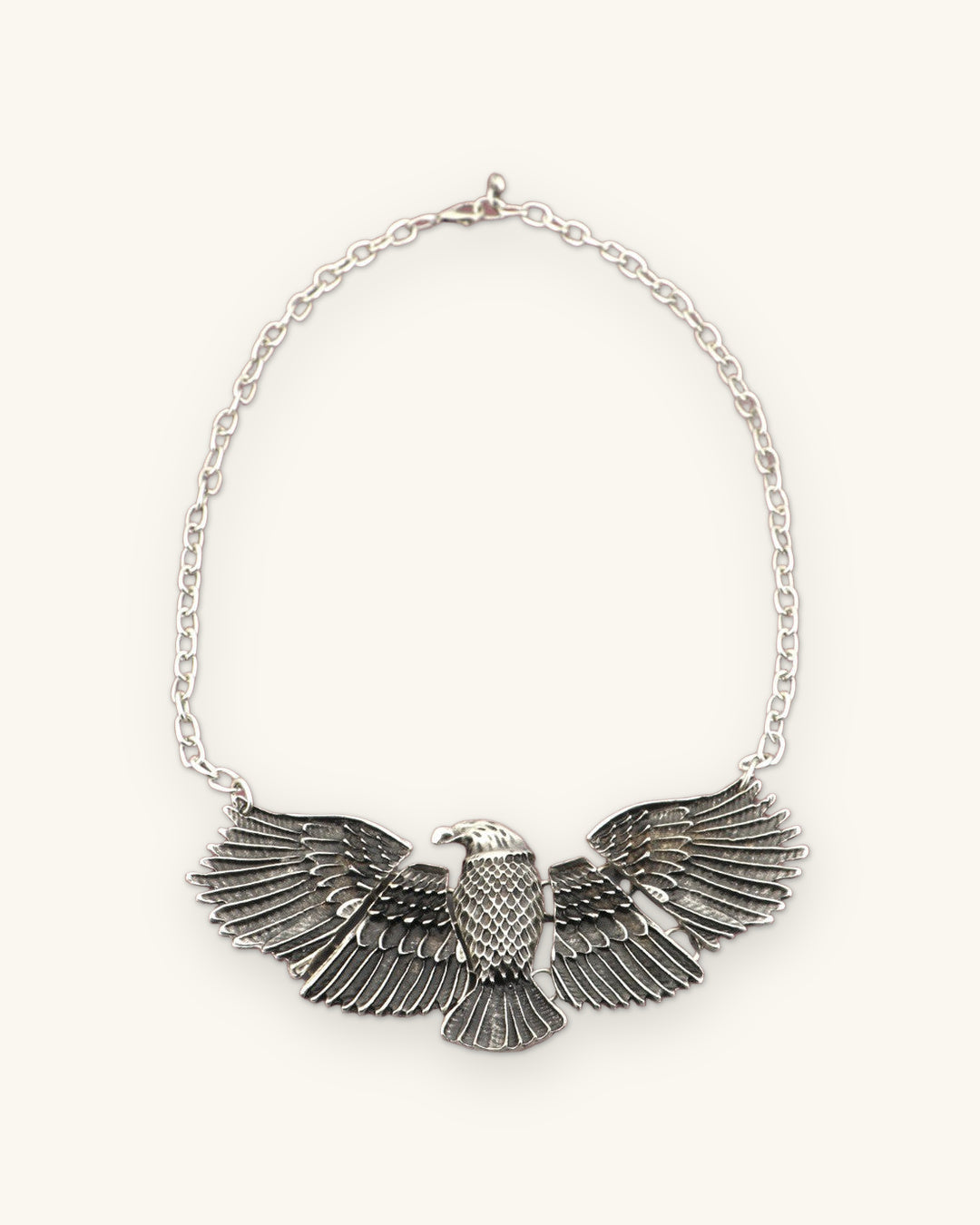 Eagle pendant necklace laid flat with the full cable chain and clasp, front view, shown on a sand background