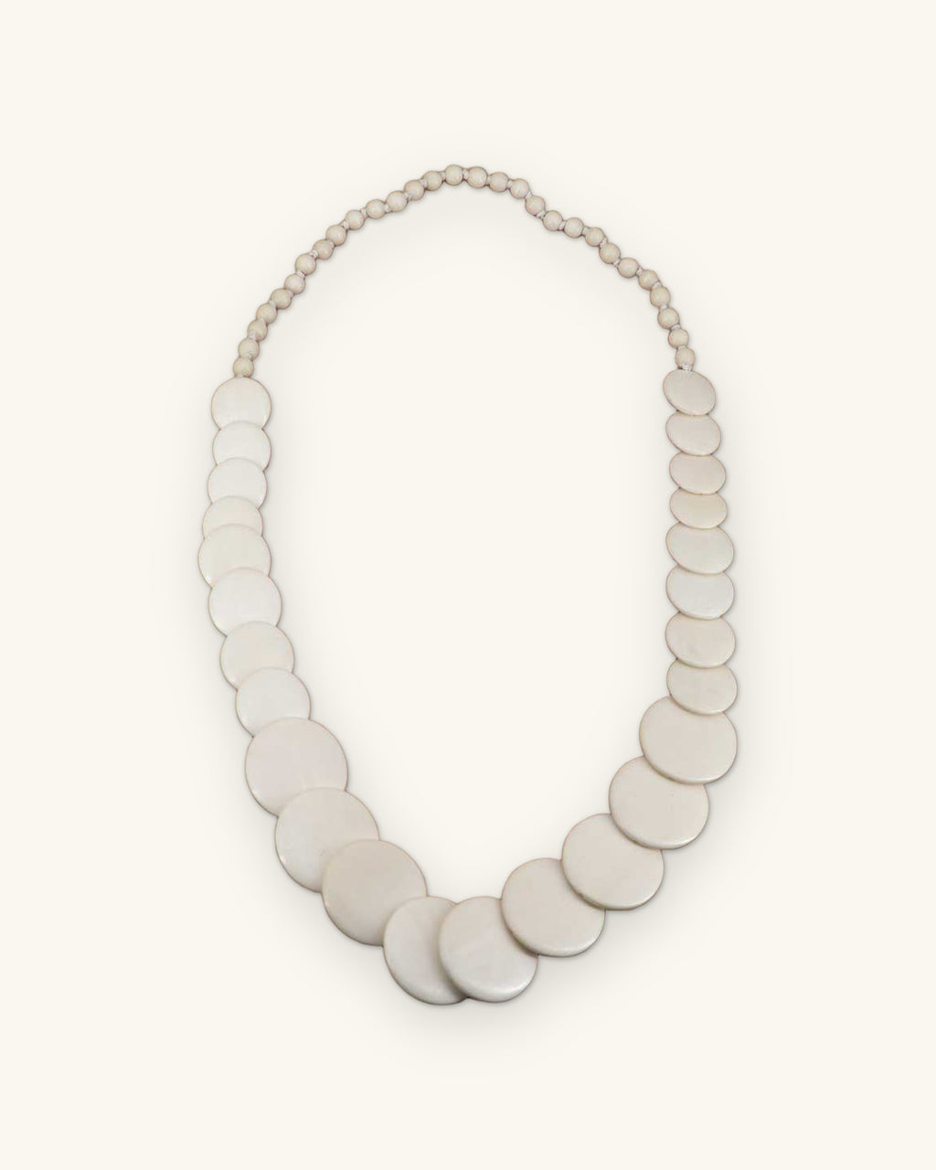Cascading white wood disk necklace with graduated discs and small round beads, made in the Philippines, shown on a sand background