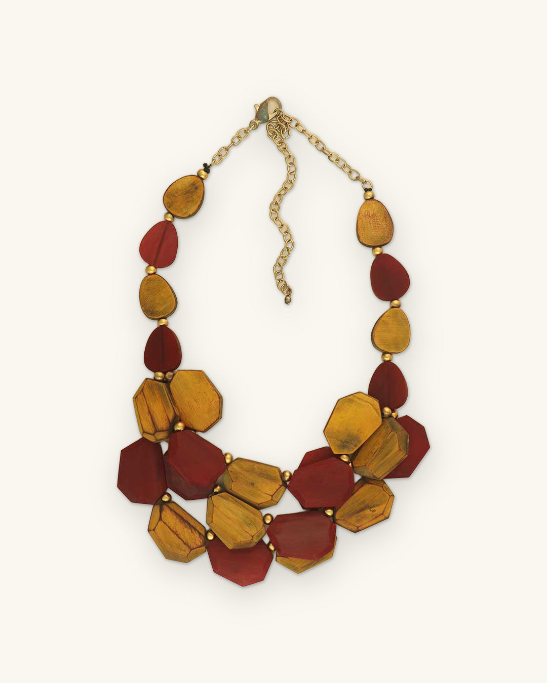 Two-tier bib necklace of amber and crimson dyed horn pieces with brass beads and chain, made in India, shown on a sand background